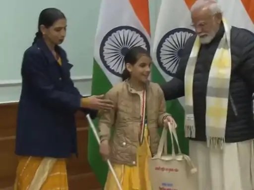 Garima, holding a white cane and her Bal Puraskar tote bag, with Prime Minister Narendra Modi